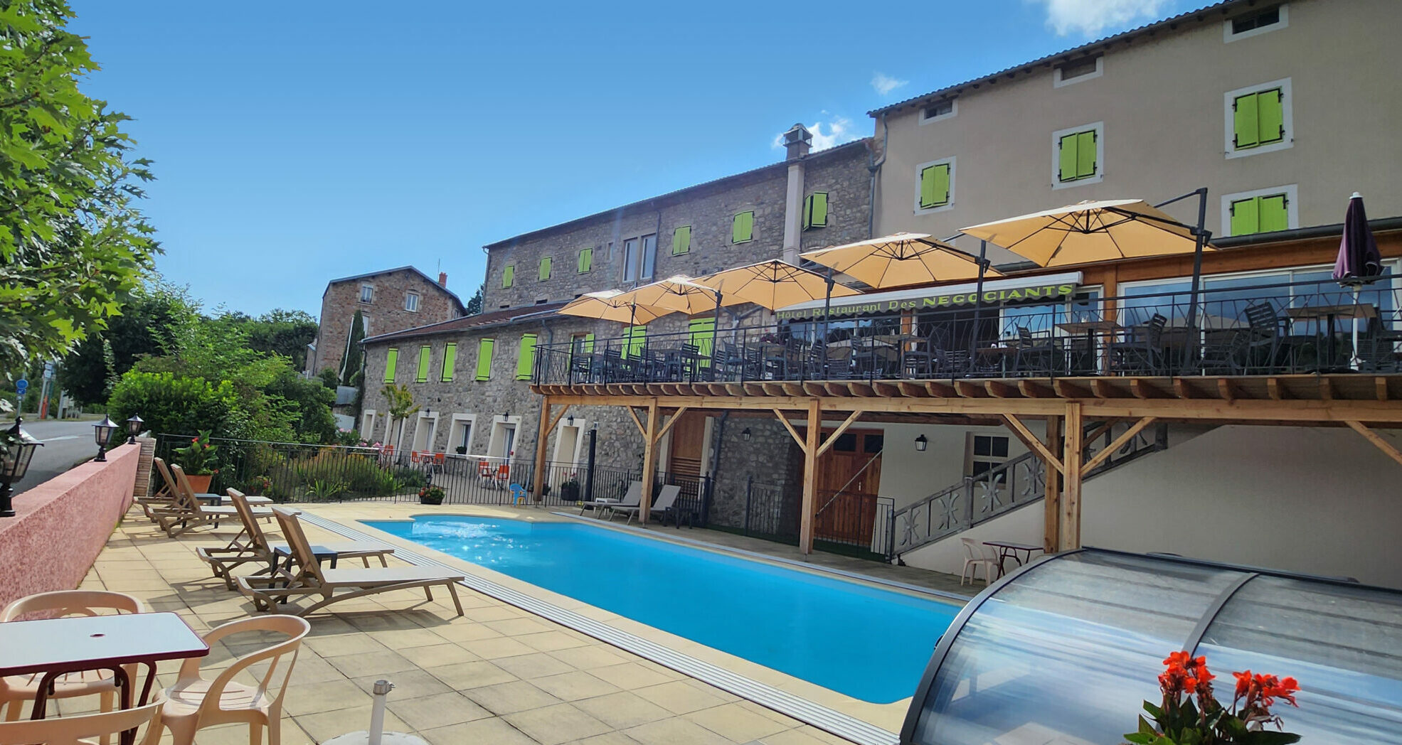 Façade de l’hôtel des négociant avec vue sur la piscine et la terrasse du restaurant sous un ciel bleu